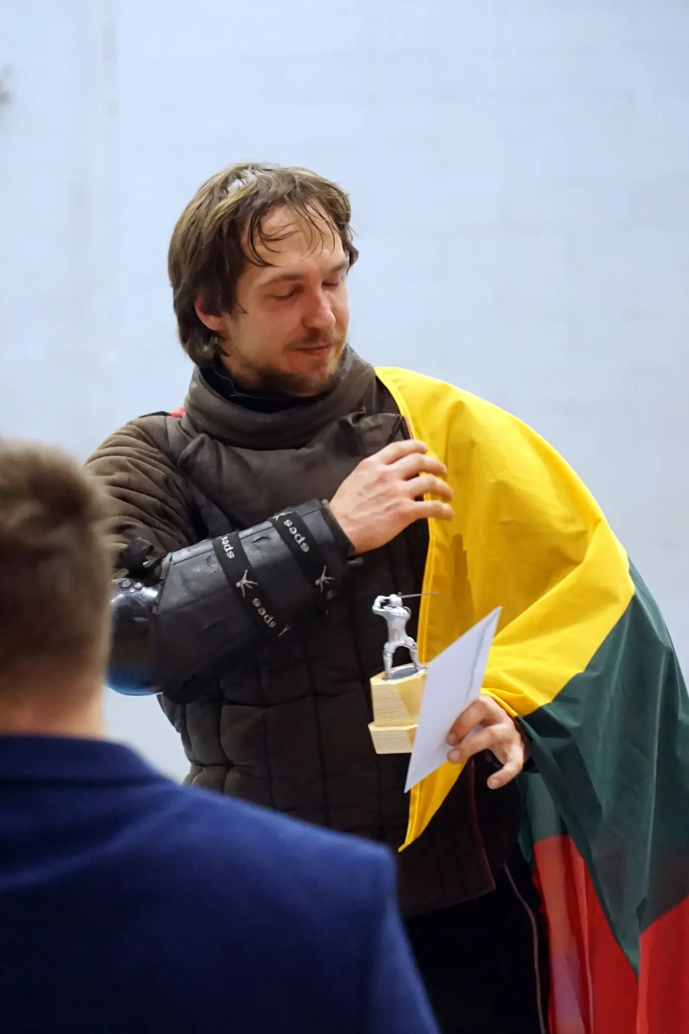 Fechtuotojas su Lietuvos vėliava ant pečių atsiima turnyro apdovanojimą